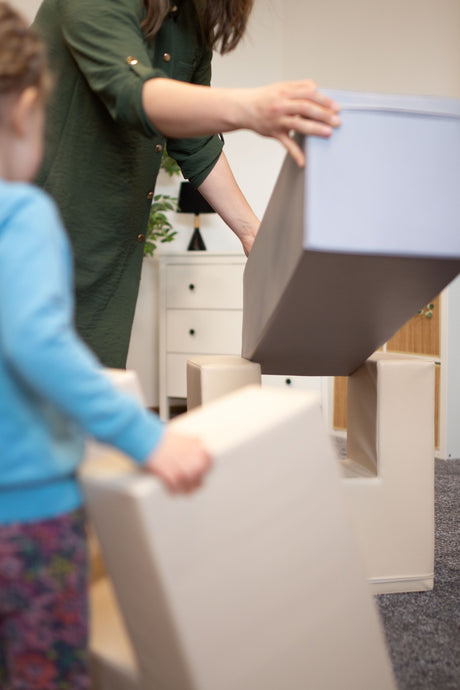 Erwachsene und Kind stapeln große, weiche Bauklötze in einem Raum