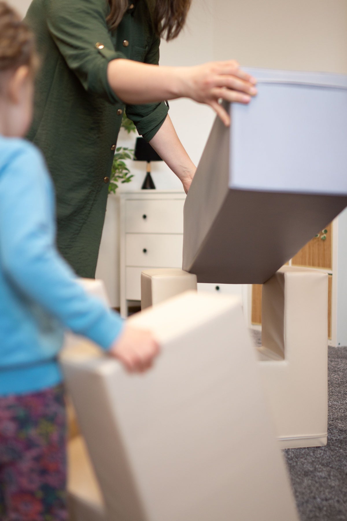 Erwachsene und Kind stapeln große, weiche Bauklötze in einem Raum