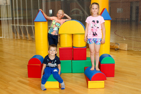 Drei Kinder spielen mit bunten Bauklötzen in einer Sporthalle