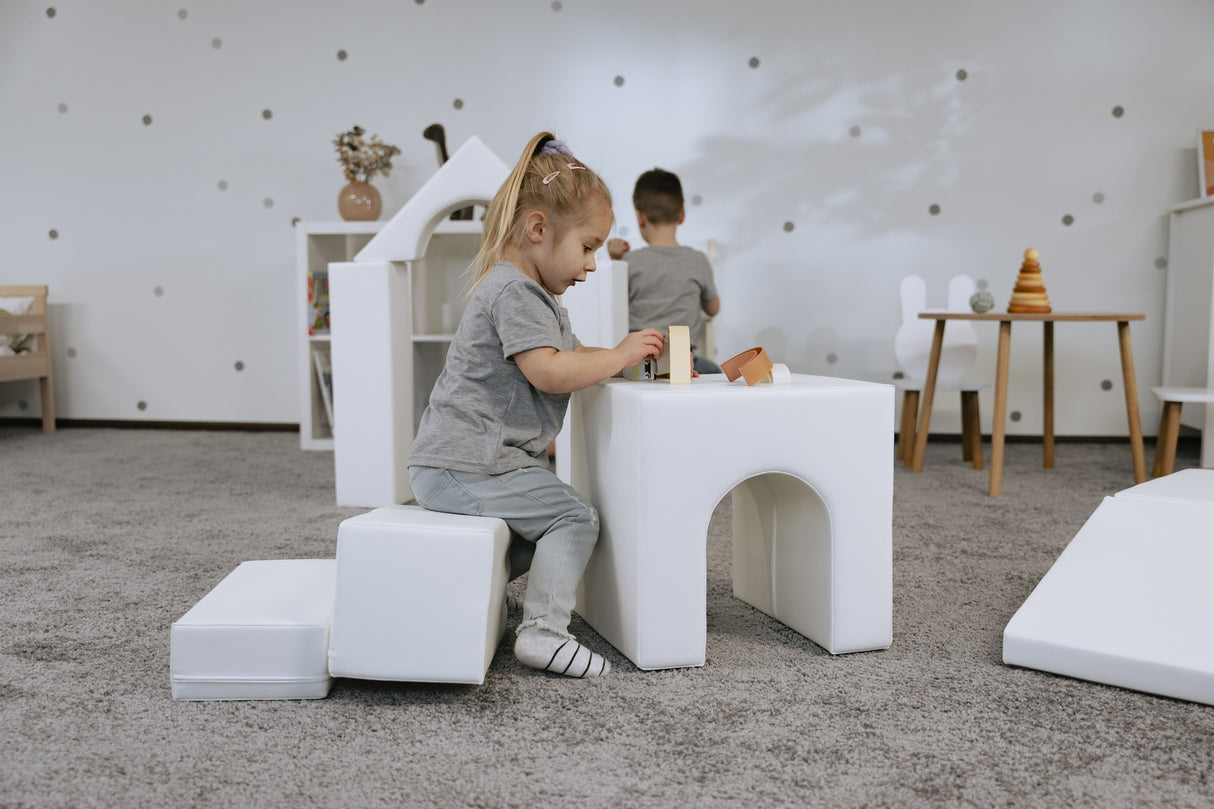 Kinder spielen an einem weißen Tisch mit Bauklötzen auf einem Teppich
