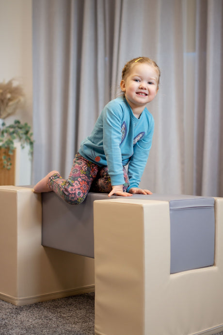 Mädchen spielt auf einem gepolsterten Spielblock in einem hellen Raum