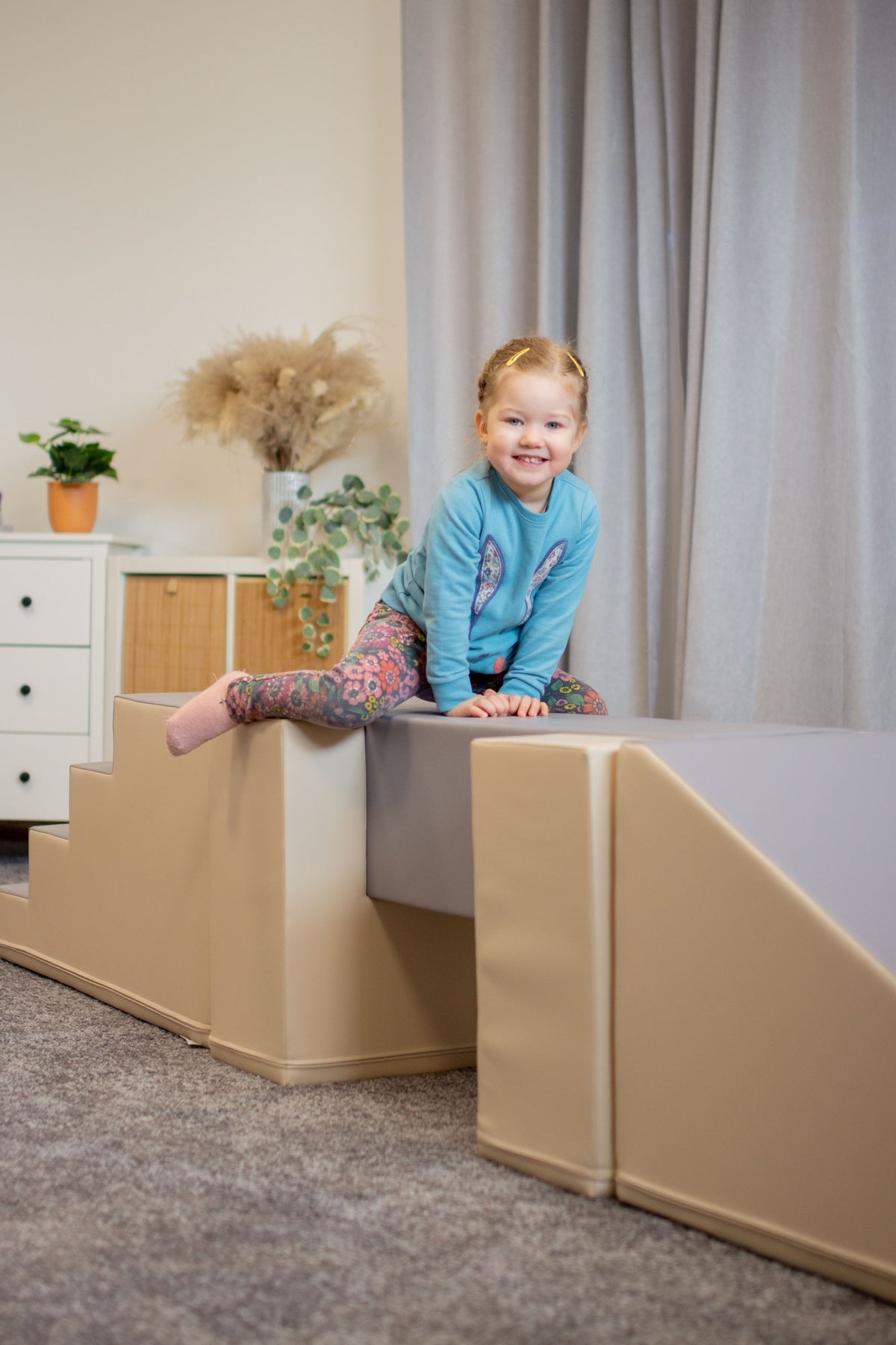 Kind sitzt auf einer gepolsterten Spielstruktur in einem hellen Raum