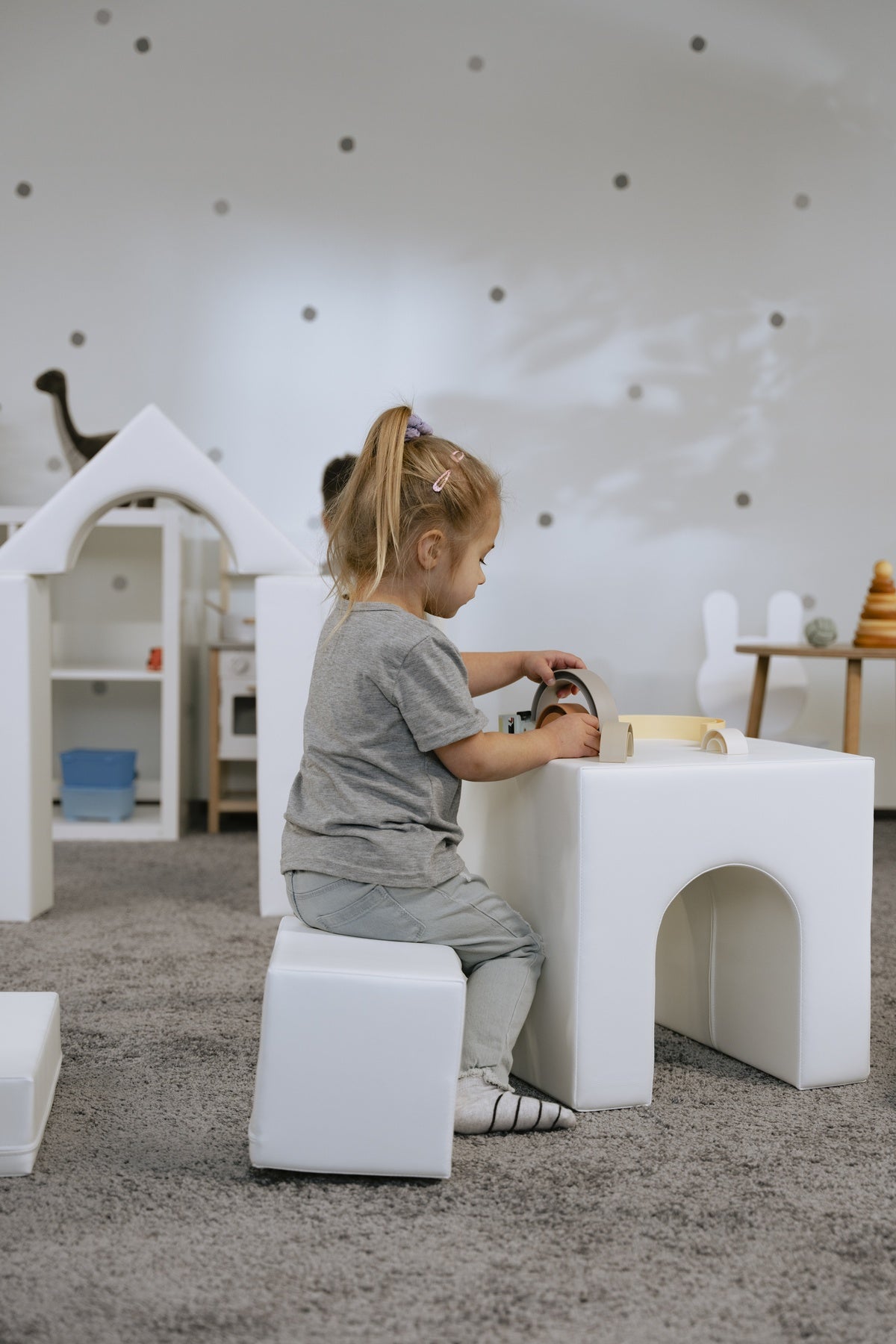 Kleines Kind spielt an einem weißen Tisch mit Spielzeug in einem Spielzimmer