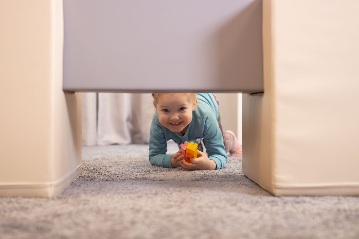Lächelndes Kind krabbelt unter einem Möbelstück mit Spielzeug in der Hand