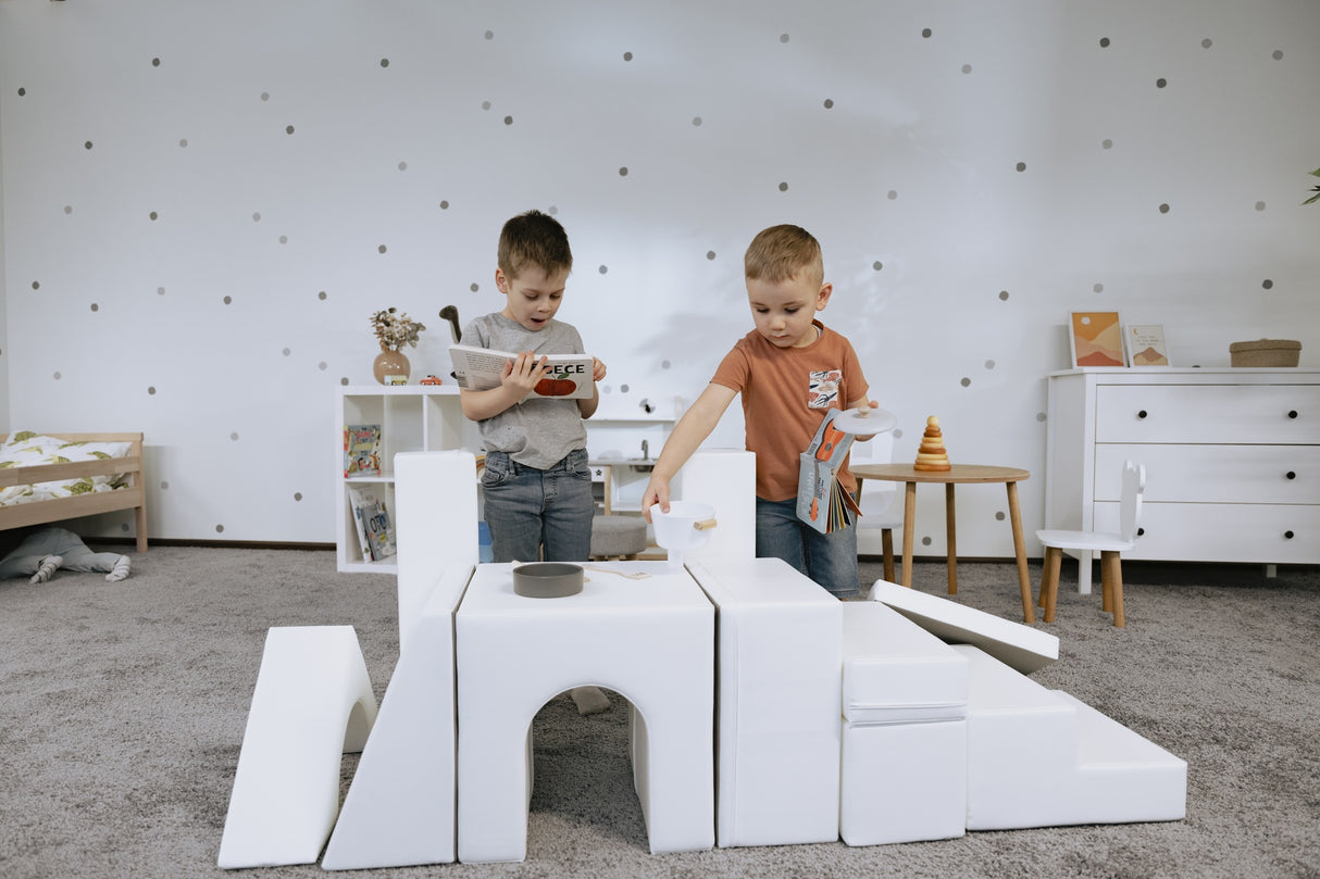 Zwei Kinder spielen mit weißen Bauklötzen auf einem Teppich