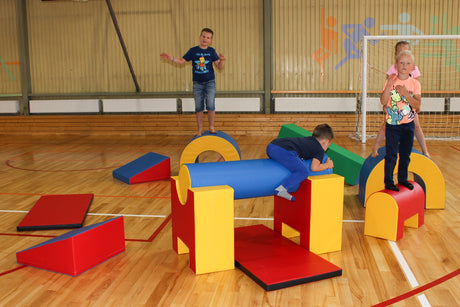 Kinder spielen auf bunten Kletterelementen in einer Sporthalle