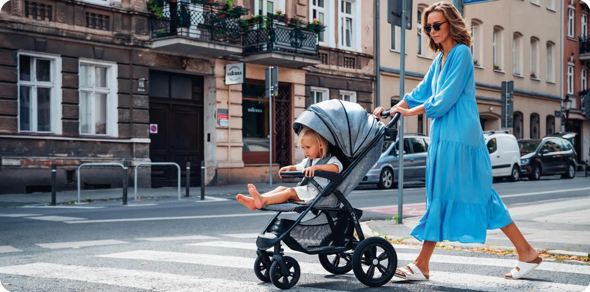 Frau schiebt Kinderwagen mit sitzendem Kind über Zebrastreifen in der Stadt
