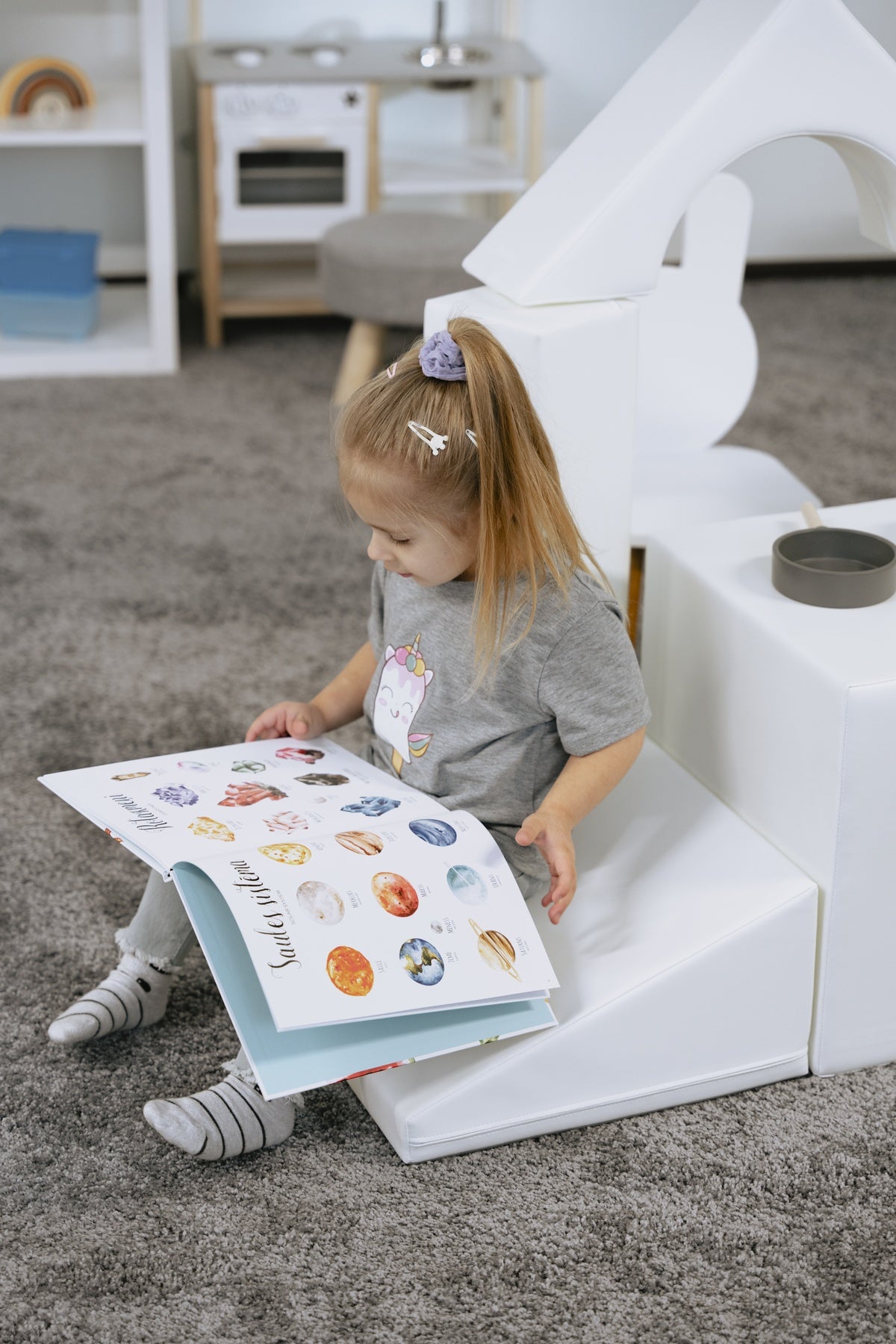 Kleines Mädchen sitzt auf Spielzeug und liest ein Bilderbuch