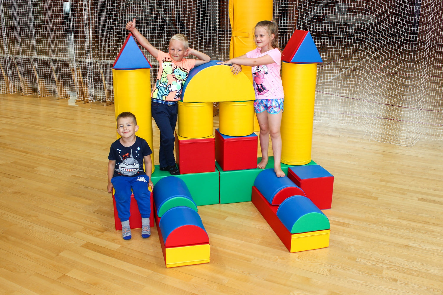 Drei Kinder spielen mit bunten Schaumstoffbausteinen in einer Sporthalle