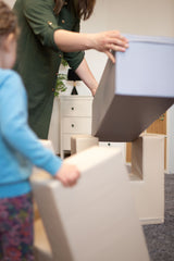 Erwachsene und Kind stapeln große, weiche Bauklötze in einem Raum