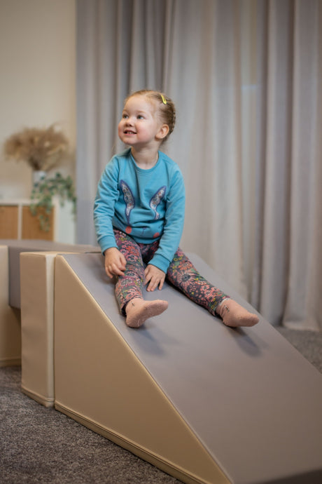 Kleines Kind sitzt auf einer Rutsche aus weichem Material