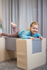 Kind liegt spielend auf einem gepolsterten Möbelstück in neutralen Farben