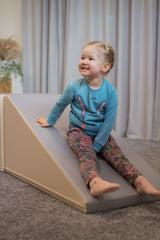 Mädchen sitzt lächelnd auf einer schrägen Spielmatte in einem Wohnraum