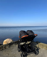 Zwillingskinderwagen am Ufer eines ruhigen Sees unter blauem Himmel
