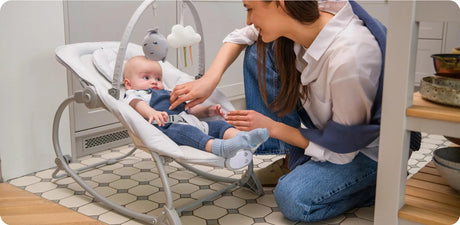 Frau spielt mit Baby in einem Wippstuhl in heller Küche