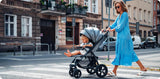 Frau schiebt Kinderwagen mit sitzendem Kind über Zebrastreifen in der Stadt