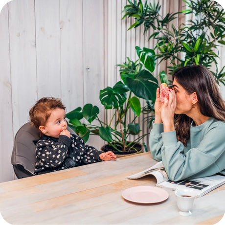 Mutter spielt mit ihrem Kind am Tisch, umgeben von Pflanzen