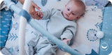 Baby in hellblauem Outfit spielt auf einer bunten Spielmatte