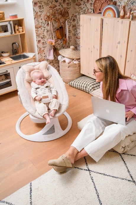 Frau sitzt am Boden und schaut auf lächelndes Baby im Schaukelstuhl