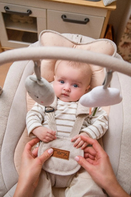 Baby in einem Schaukelstuhl mit Spielzeuganhängern und Sicherheitsgurt