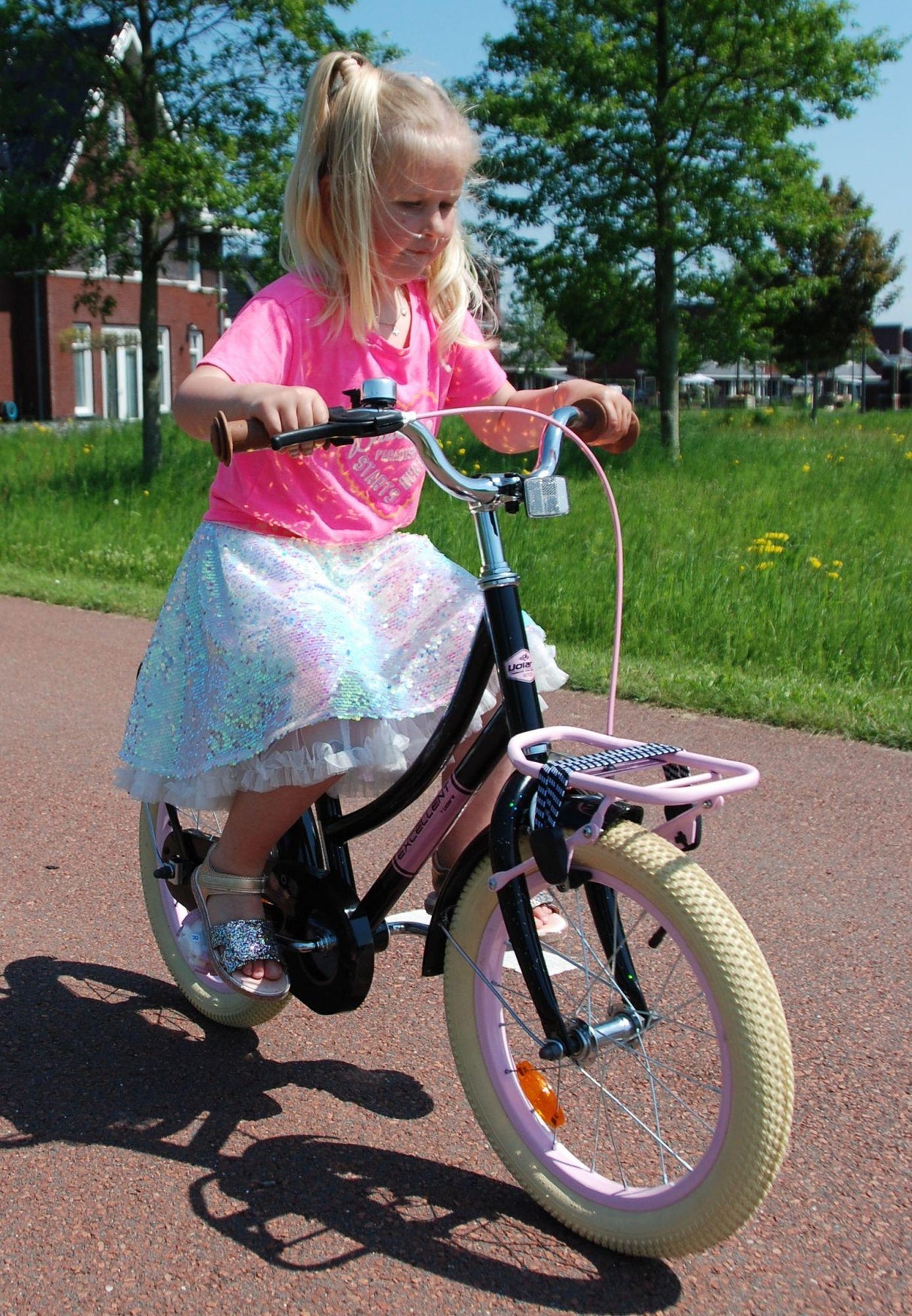 Mädchen fährt auf einem Fahrrad mit pinkem Rock und glitzerndem Oberteil