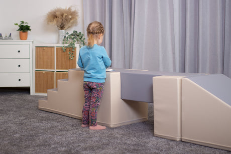 Kind steht an einer Spiel- und Kletterlandschaft mit Treppe und Plattform